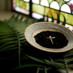 A bowl of ashes with a cross placed on them, surrounded by palm leaves.